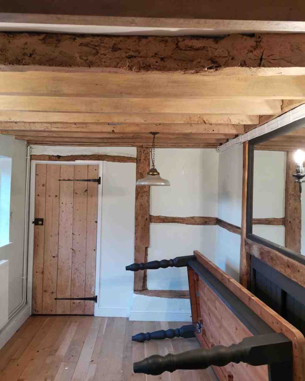 A timber-framed room with exposed oak ceiling beams and wall studs in a natural oak tone
